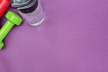 Image showing Ladie's dumbbells and water bottle over purple fitness mat, top view.