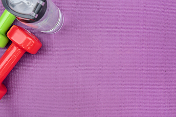 Image showing Ladie's dumbbells and water bottle over purple fitness mat, top view.