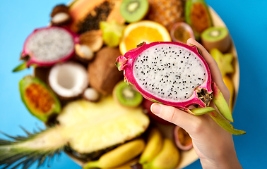 Image showing hand holding half of dragon fruit over blue