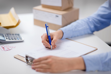 Image showing woman with clipboard and parcels at post office