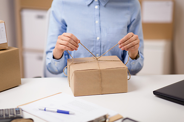 Image showing woman packing parcel and tying rope at post office