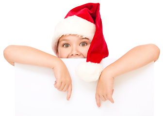 Image showing Little girl in santa hat is holding blank board