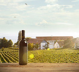 Image showing Bottle of wine on wooden rail with country rural scene in background