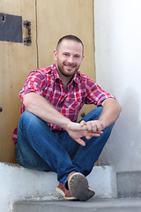 Image showing young bearded man sitting at a door