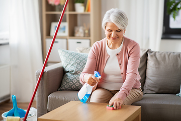 Image showing senior woman with detergent cleaning table at home