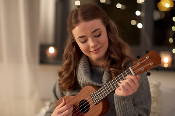 Image showing happy young woman playing ukulele guitar at home