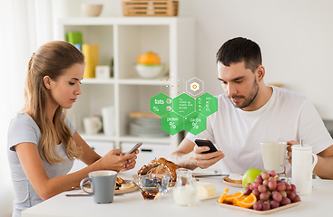 Image showing couple with smartphones having breakfast at home