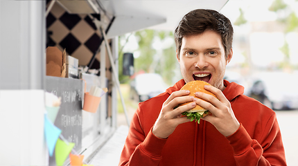 Image showing happy young man eating hamburger at food truck