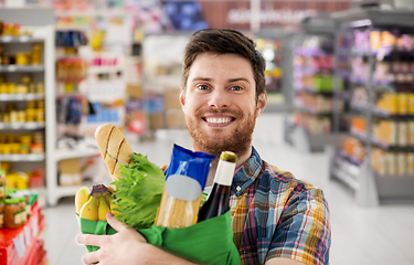 Image showing smiling young man with food in bag at supermarket