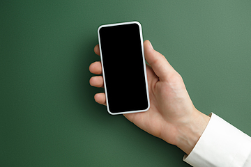 Image showing Male hand holding smartphone with empty screen on green background for text or design