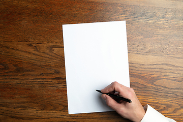 Image showing Male hand holding pen and writing on empty sheet on wooden background for text or design