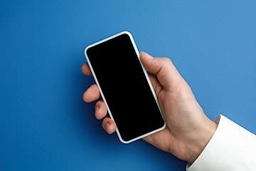 Image showing Male hand holding smartphone with empty screen on blue background for text or design