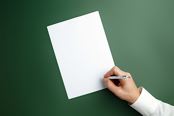 Image showing Male hand holding pen and writing on empty sheet on green background for text or design