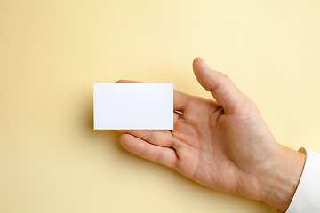 Image showing Male hand holding a blank business card on soft yellow background for text or design