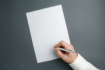 Image showing Male hand holding pen and writing on empty sheet on grey background for text or design