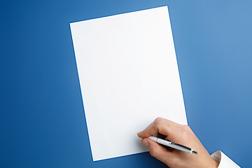 Image showing Male hand holding pen and writing on empty sheet on blue background for text or design