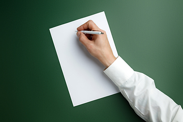 Image showing Male hand holding pen and writing on empty sheet on green background for text or design