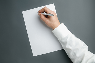 Image showing Male hand holding pen and writing on empty sheet on grey background for text or design
