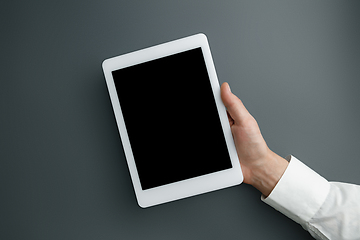 Image showing Male hand holding tablet with empty screen on grey background for text or design