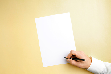 Image showing Male hand holding pen and writing on empty sheet on yellow background for text or design