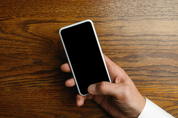 Image showing Male hand holding smartphone with empty screen on wooden background for text or design