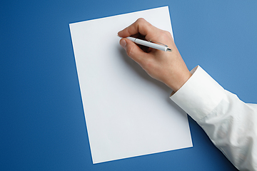 Image showing Male hand holding pen and writing on empty sheet on blue background for text or design