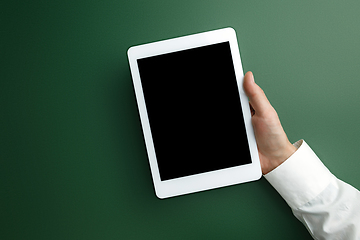 Image showing Male hand holding tablet with empty screen on green background for text or design