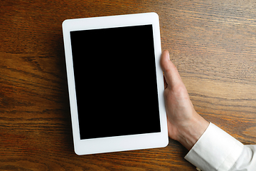 Image showing Male hand holding tablet with empty screen on wooden background for text or design