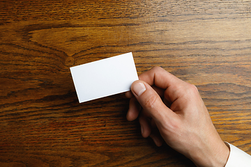 Image showing Male hand holding a blank business card on wooden background for text or design