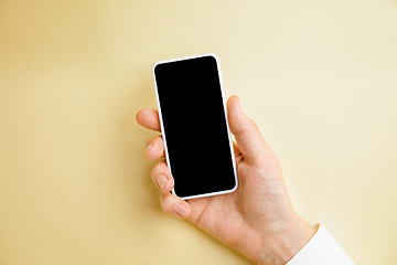 Image showing Male hand holding smartphone with empty screen on yellow background for text or design