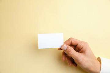 Image showing Male hand holding a blank business card on soft yellow background for text or design