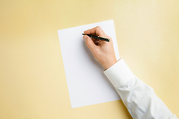 Image showing Male hand holding pen and writing on empty sheet on yellow background for text or design