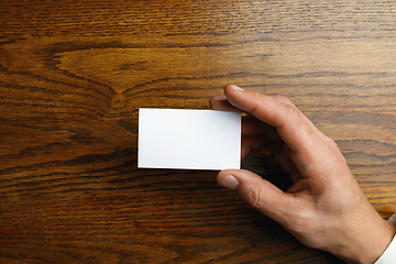 Image showing Male hand holding a blank business card on wooden background for text or design