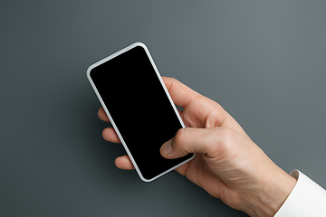 Image showing Male hand holding smartphone with empty screen on grey background for text or design