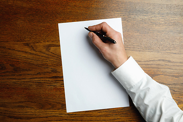 Image showing Male hand holding pen and writing on empty sheet on wooden background for text or design