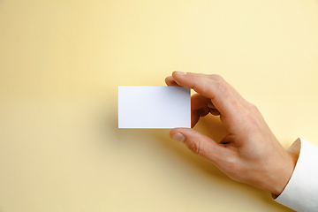 Image showing Male hand holding a blank business card on soft yellow background for text or design