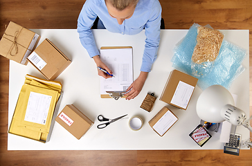 Image showing woman with clipboard and parcels at post office