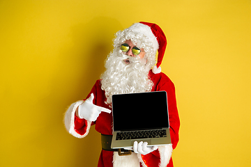 Image showing Santa Claus with modern gadgets isolated on yellow studio background