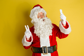 Image showing Santa Claus with modern gadgets isolated on yellow studio background