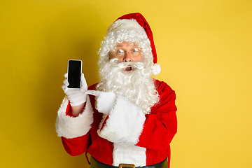 Image showing Santa Claus with modern gadgets isolated on yellow studio background