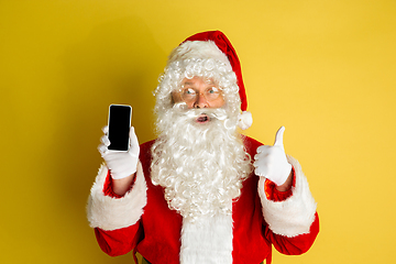 Image showing Santa Claus with modern gadgets isolated on yellow studio background