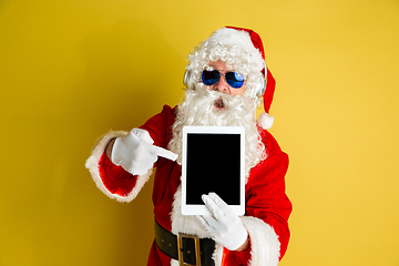 Image showing Santa Claus with modern gadgets isolated on yellow studio background