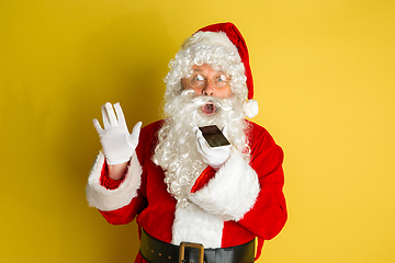 Image showing Santa Claus with modern gadgets isolated on yellow studio background