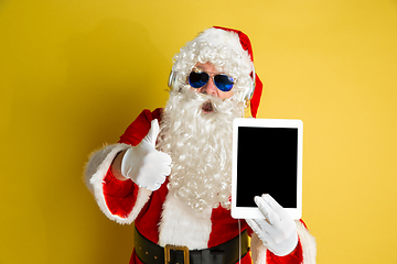 Image showing Santa Claus with modern gadgets isolated on yellow studio background