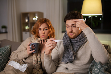 Image showing sick couple with thermometer and tea at home