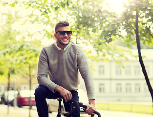 Image showing young man in shades riding bicycle on city street