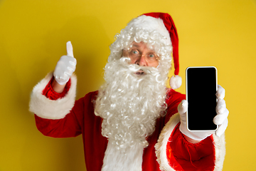 Image showing Santa Claus with modern gadgets isolated on yellow studio background