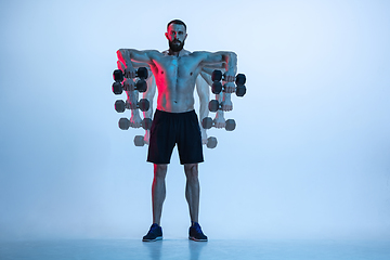 Image showing Young caucasian bodybuilder training over blue background