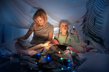 Image showing Mother and daughter sitting in a teepee, reading stories with the flashlight
