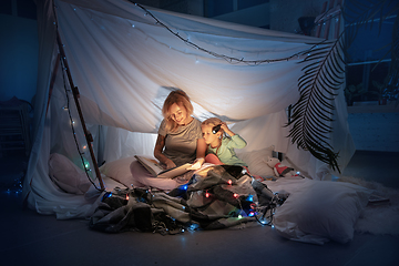 Image showing Mother and daughter sitting in a teepee, reading stories with the flashlight